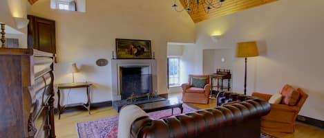 A spacious living room with a fireplace, a leather sofa, a patterned rug, and a chandelier.