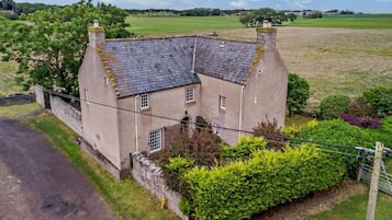 A two-story house with a stone facade, a sloped roof, and a small garden with a hedge.