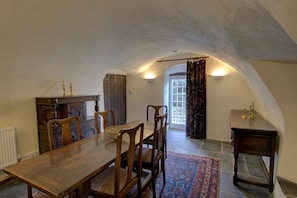 A dining area with a wooden table and chairs, a patterned rug, and a view through an arched doorway to a window with curtains. - Little Tarrel Castle Portmahomack (Tain)