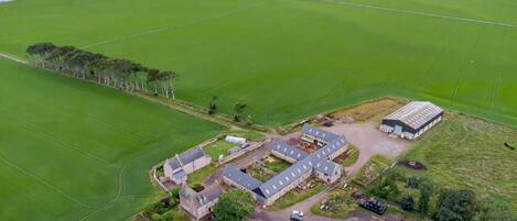 An aerial view of a rural property with multiple buildings, green fields, and a coastline in the background.