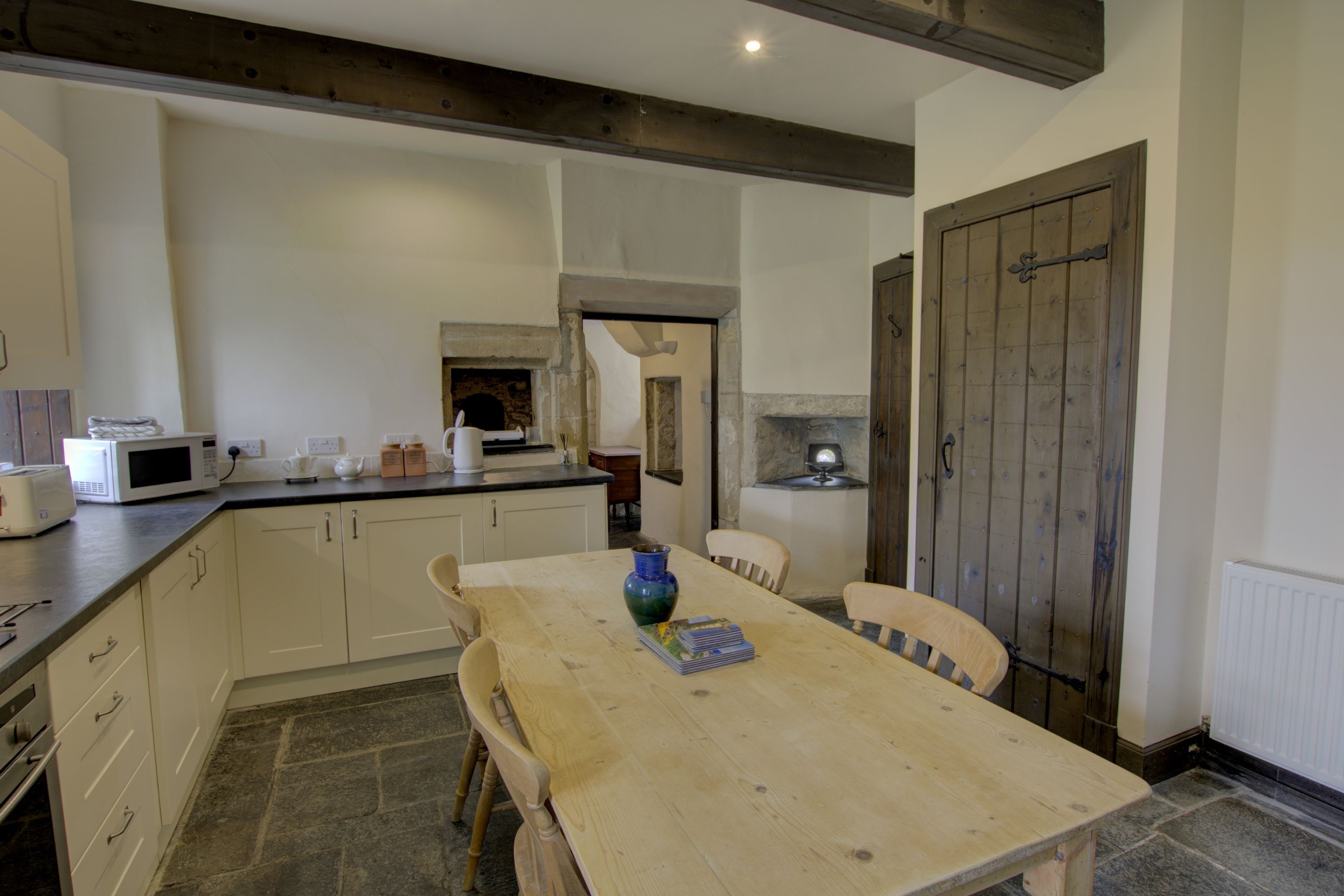 A kitchen with a wooden table, chairs, a microwave, and a stone floor.