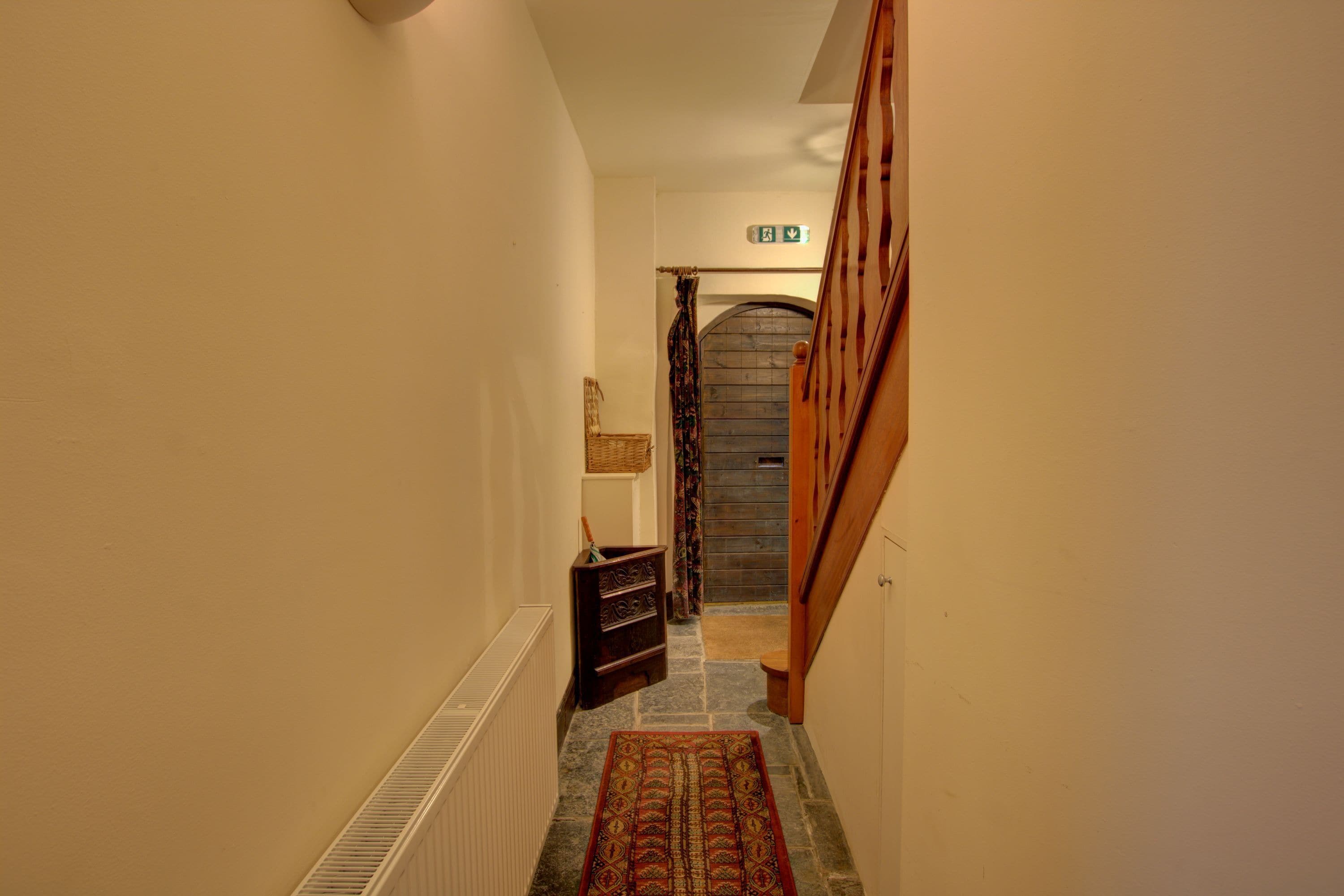 A narrow hallway with a patterned rug, a wooden bench, and a door at the end.