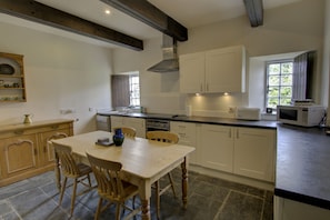 A kitchen with a dining table, chairs, white cabinets, a microwave, and a window with a view of greenery. - Little Tarrel Castle Portmahomack (Tain)