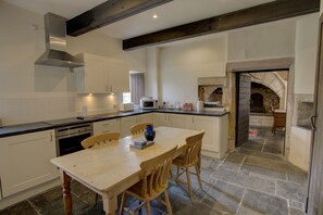 A kitchen with a wooden table, chairs, and a stone fireplace. - Little Tarrel Castle Portmahomack (Tain)