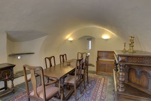 A dining room with a long wooden table, chairs, a patterned rug, and a wooden cabinet with a brass candelabra. - Little Tarrel Castle Portmahomack (Tain)