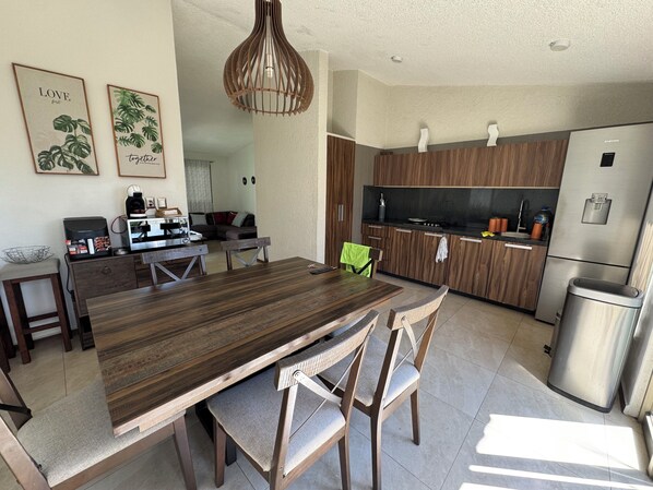 A modern kitchen with wooden cabinets, a stainless steel refrigerator, and a dining area with a wooden table and chairs.