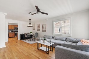 A modern living room with a grey sofa, a coffee table, and a dining area with a table and chairs. - Haya Hideaway - Central - Cozy & Quiet (Tampa)