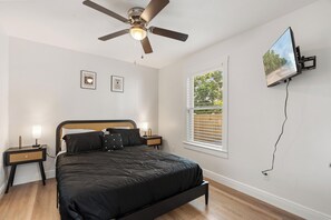 A bedroom with a bed, a ceiling fan, a TV mounted on the wall, and a window with blinds. - Haya Hideaway - Central - Cozy & Quiet (Tampa)