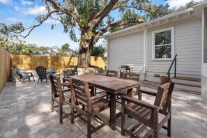 Eine Terrasse mit Holztisch und -stühlen, einem Grill und einem großen Baum.