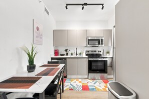 A compact kitchen with modern appliances, a dining area with a table and chairs, and a small seating area with a bench. - Cozy Fun and Vibrant Central Wynwood! King Bed! (Miami)