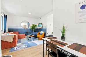 A modern living room with a sofa, armchair, and a dining table with chairs. There is a mirror on the wall and a potted plant on the table. - Cozy Fun and Vibrant Central Wynwood! King Bed! (Miami)