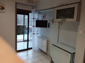 Ein Zimmer mit einer Schiebetür zum Außenbereich, einem weißen Heizkörper, einem an der Wand montierten Fernseher und einem kleinen Schrank.
