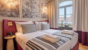 A hotel room with a large bed, two bedside tables, a nightstand, a window with curtains, and wall art. - Augusta Grand Hotel (Lisbon)