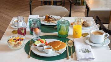 A breakfast setting with a plate of pancakes, a glass of orange juice, a bowl of fruit, and a cup of coffee.