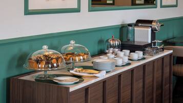 A buffet setup with covered dishes, plates, and a coffee machine.