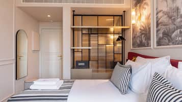 Habitación de hotel con cama, mesita de noche, espejo, armario, estante con objetos decorativos y lámpara de pared.
