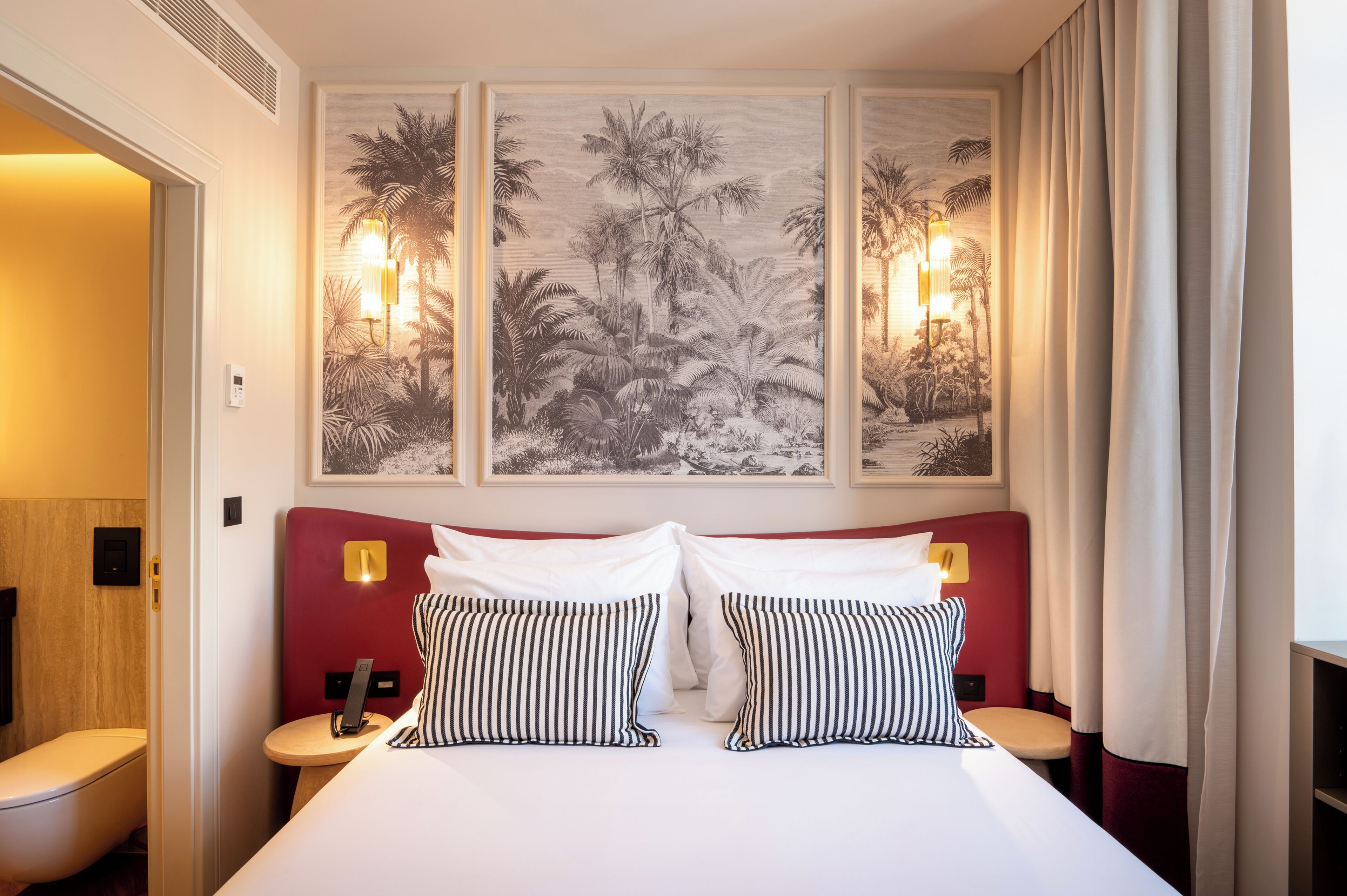 A hotel room with a large bed, two bedside tables, a wall-mounted light, and a painting above the bed.
