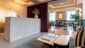 A hotel reception area with a marble counter, a vase with flowers, and a seating area with tables and chairs. - Augusta Grand Hotel (Lisbon)