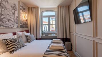 A hotel room with a large bed, a flat-screen TV, a window with curtains, and a wall-mounted artwork.