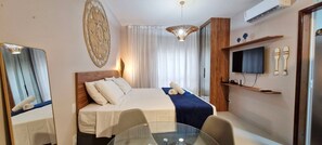 A hotel room with a bed, a TV, a mirror, a glass table, and a ceiling light. - COPFL0110 - Cond Recanto do Flamengo (Salvador)