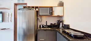 Eine kleine Küchenzeile mit Kühlschrank, Mikrowelle, Kaffeemaschine und Spüle.