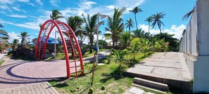 A red metal structure, possibly a water slide, in a landscaped area with palm trees and a paved walkway. - COPFL0110 - Cond Recanto do Flamengo (Salvador)