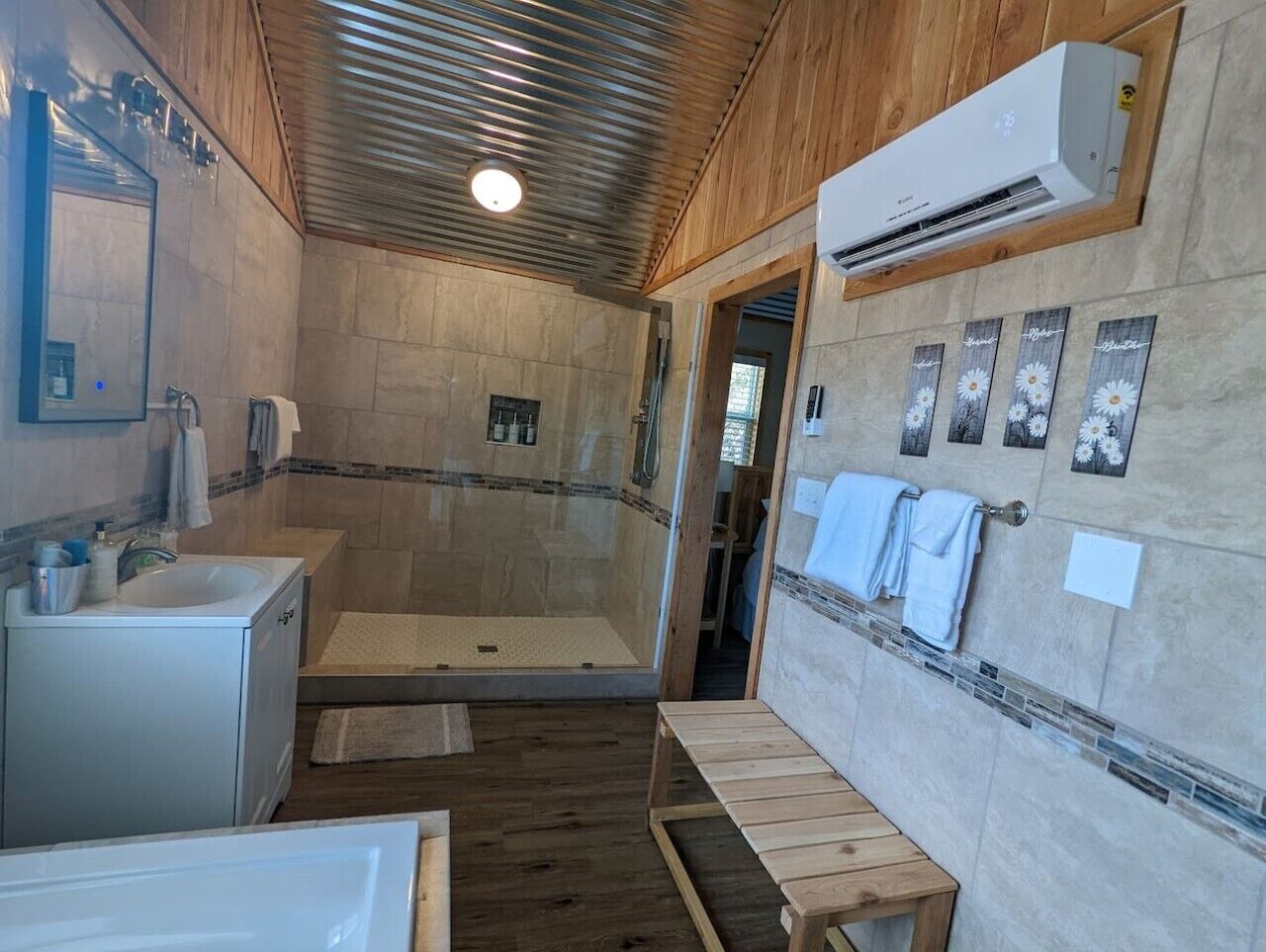 A bathroom with a shower, a sink, and a bench.