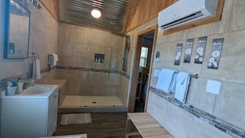 A bathroom with a shower, a sink, and a bench.