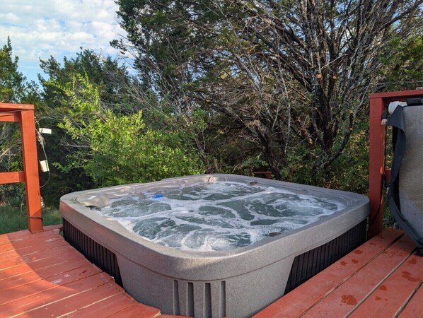 Un jacuzzi en una terraza de madera con árboles al fondo.