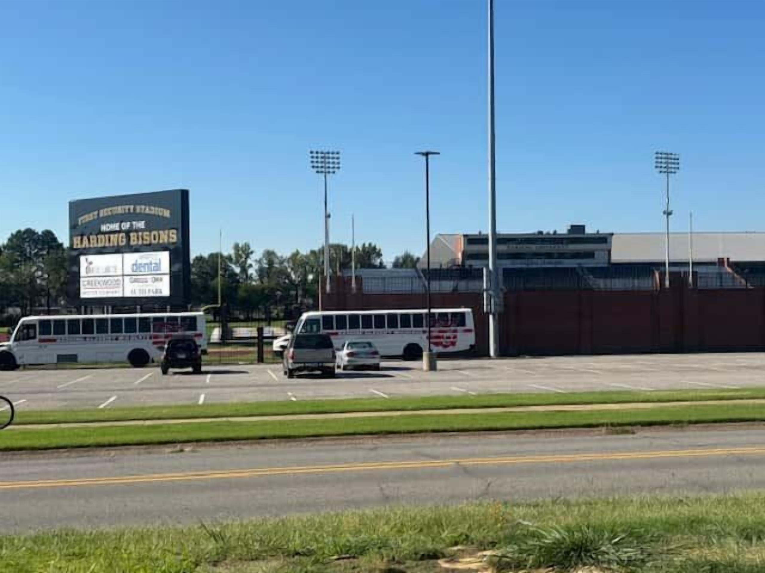 A parking lot with vehicles, a large sign for a stadium, and a building with a flat roof.