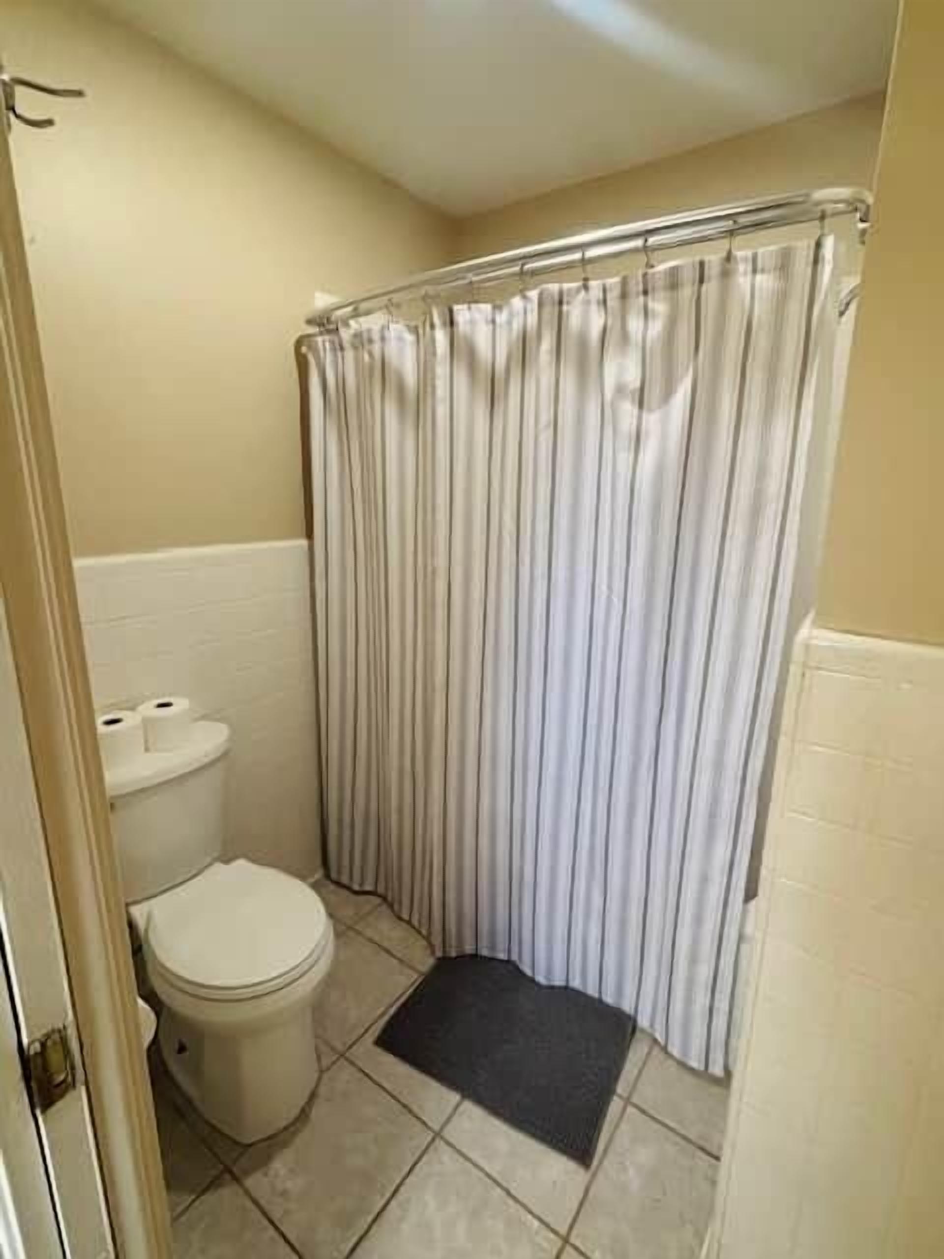 Un baño con inodoro, cortina de ducha y un tapete.