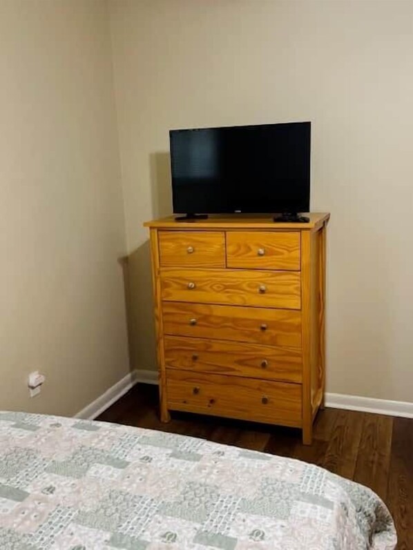 A wooden dresser with a flat-screen TV on top, positioned against a wall in a room with a patterned bedspread.
