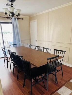 A dining area with a long wooden table surrounded by black chairs, a chandelier, and a door with a white panel.