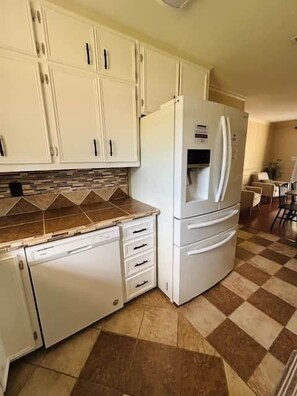 A kitchen with white cabinets, a white refrigerator, and a checkered floor.