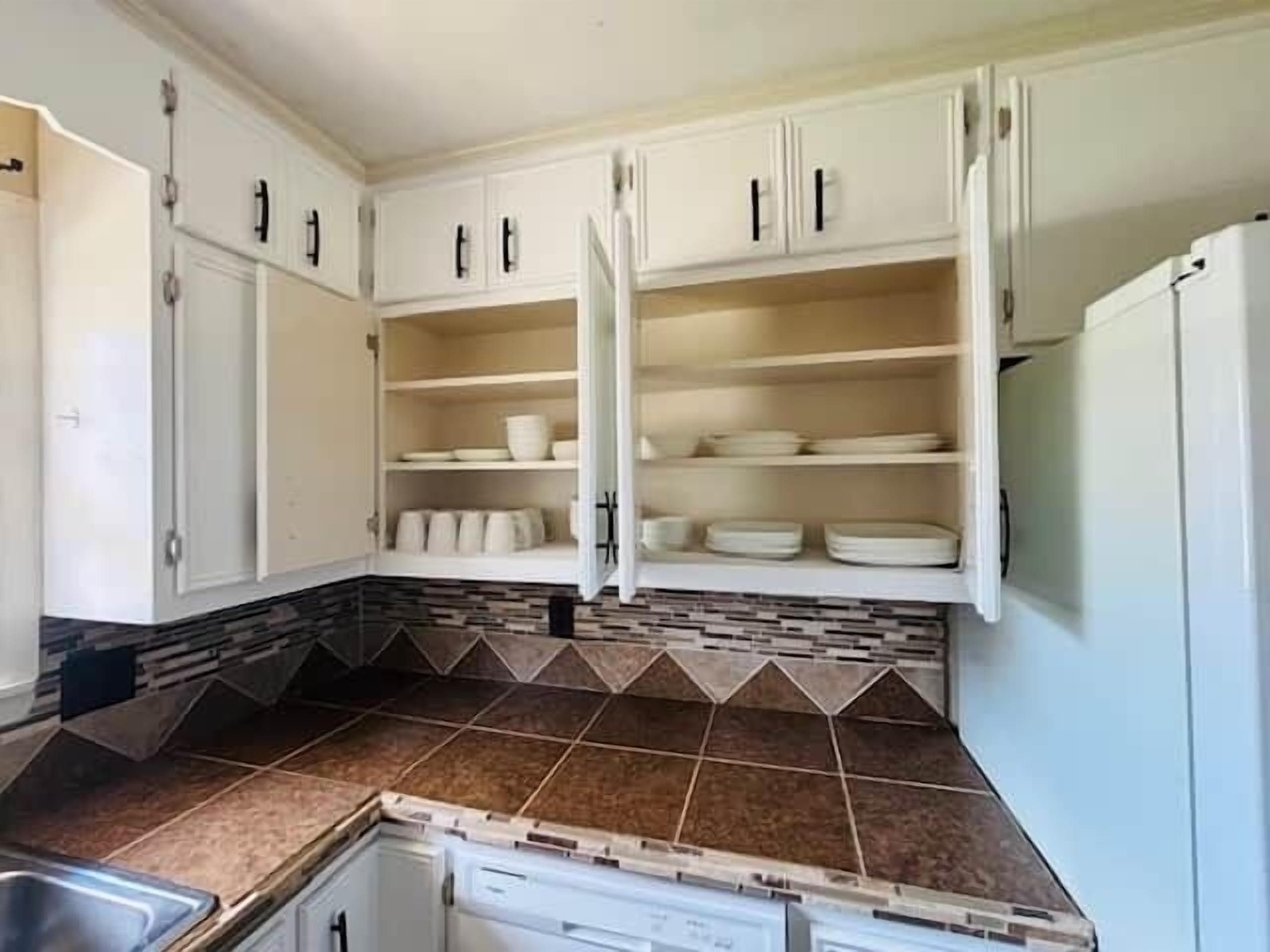 A kitchen with white cabinets, a tiled backsplash, and a built-in dishwasher.