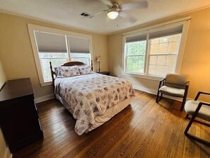 Ein Schlafzimmer mit einem Bett, zwei Fenstern, einem Deckenventilator und einem Sessel.