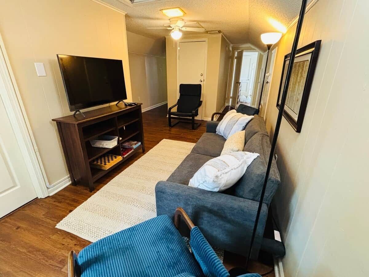 Ein Wohnzimmer mit einer Couch, einem Fernseher auf einem Schrank, einem Deckenventilator und einer Tür zu einem anderen Raum.