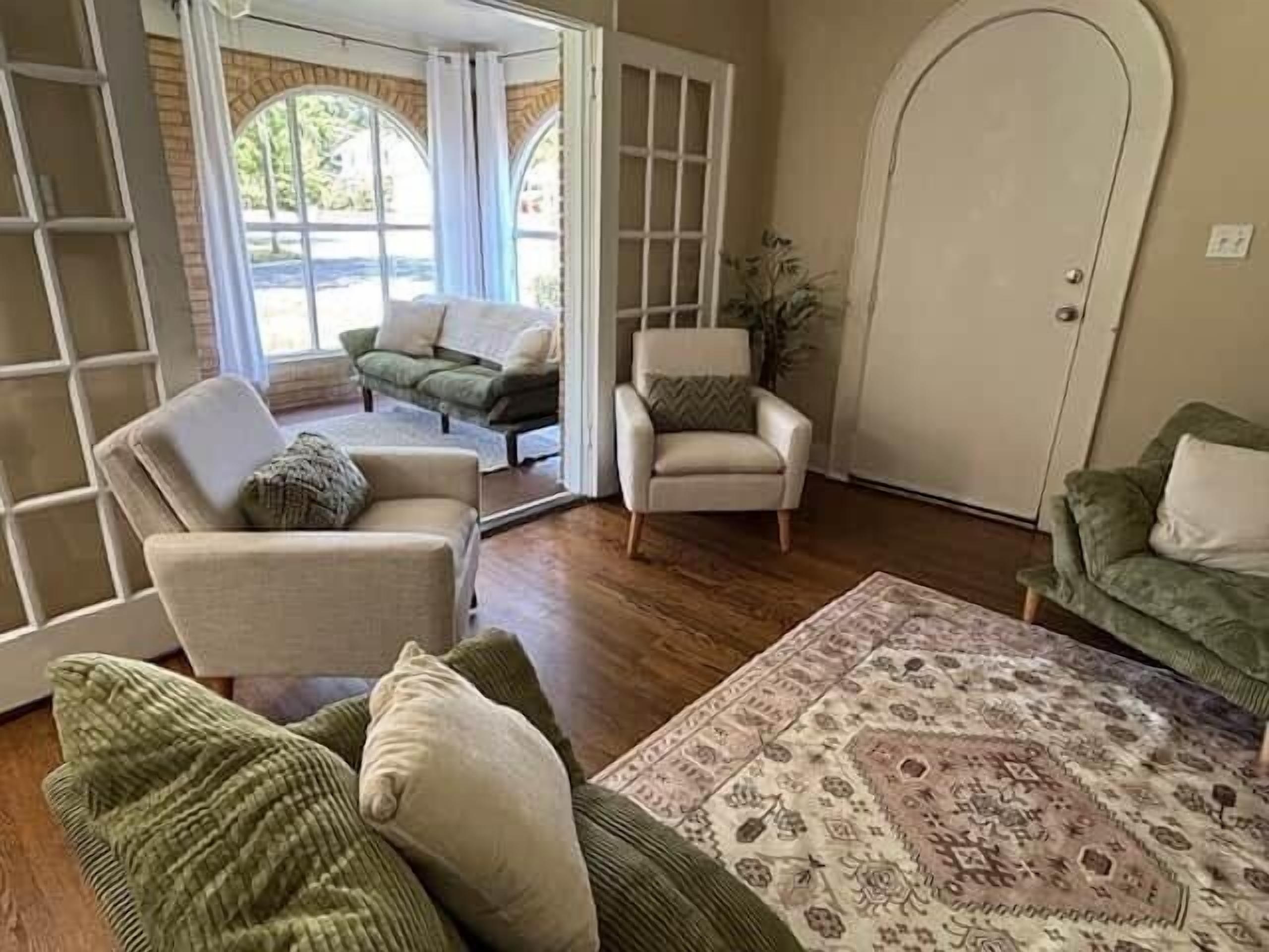 A living room with a sofa, armchairs, a patterned rug, and a door leading to an outdoor area.