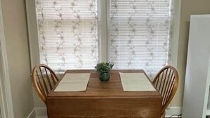 A dining table with four chairs, a potted plant, and a window with blinds. - The Alumni House at Harding (Searcy)