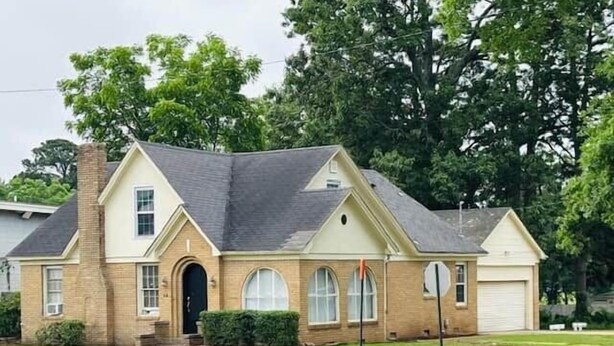 A two-story house with a brick facade, a chimney, and a garage. - The Alumni House at Harding (Searcy)