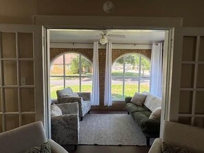 A room with a view through a door, featuring a sofa, chairs, and a rug. - The Alumni House at Harding (Searcy)