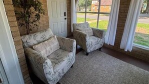A room with two patterned sofas, a door, and a large window with curtains. - The Alumni House at Harding (Searcy)