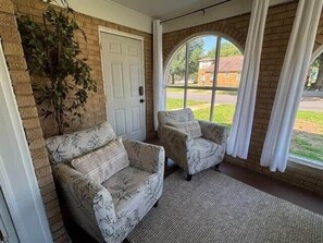 Ein Zimmer mit zwei gemusterten Sofas, einer Tür und einem großen Fenster mit Vorhängen.