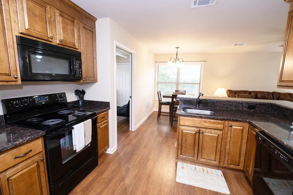 A kitchen with wooden cabinets, a black stove, a microwave, and a granite countertop.