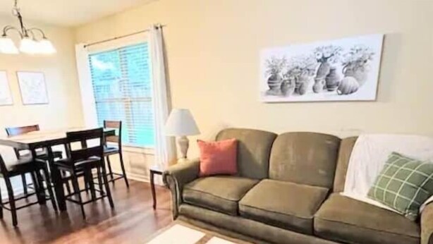 A living room with a sofa, a coffee table, a dining table with chairs, and a window with blinds.