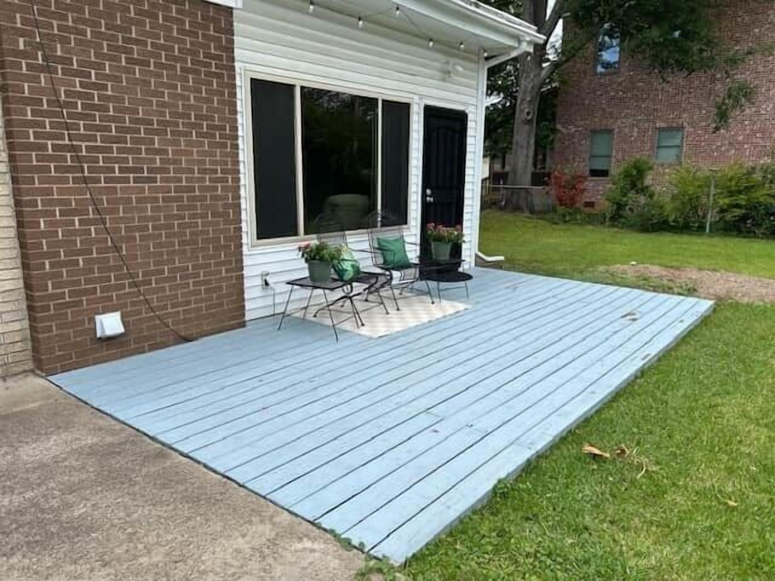 A covered patio with a blue deck, a brick wall, and a sliding glass door leading to a room.