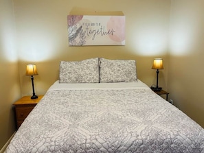 A neatly made bed with patterned bedding, two bedside lamps, and a motivational quote on the wall.