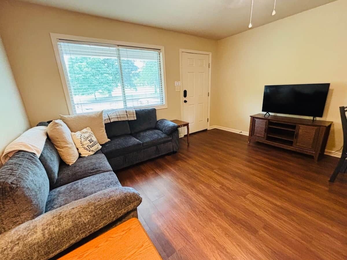 A living room with a sectional sofa, a television on a stand, and a door.