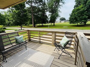A covered outdoor seating area with two metal chairs and a bench, surrounded by a wooden fence and a view of a park.