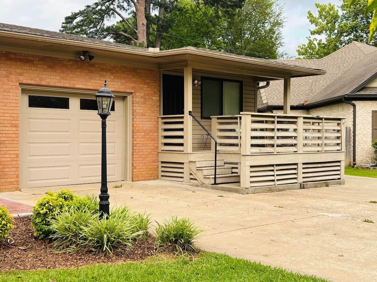 Une maison de plain-pied avec un garage, une véranda et un petit jardin devant, agrémenté d’un lampadaire.